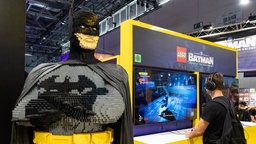 Ein Besucher spielt Legacy of the Dark Knight bei der Gamecom-Eröffnung am 20.08.2025. Dabenen steht ein großer Lego Batman.