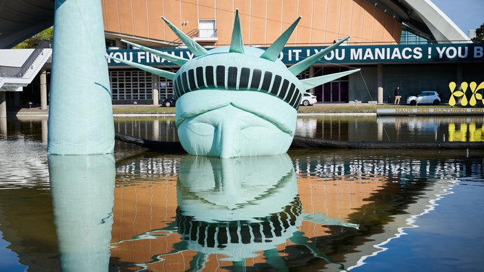 Der halbe Kopf einer aufblasbaren Freiheitsstatue, das Kunstwerk „Status of Liberty“ liegt in dem Gewässer vor dem Haus der Kulturen der Welt.