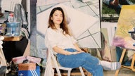 Jeehye Song sitzt in einer Jeans mit Badeschlappen auf einem Klappstuhl. Um sie herum sieht man ihre Werke.