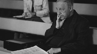 Komponist und Dirigent Pierre Boulez sitzt mit einer Partitur auf dem Schoß auf einer Bank.