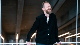 Der Komponist Øvind Torvund lehnt lächelnd an einem weißen Geländer
