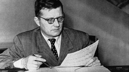 Der Komponist Dimitri Schostakowitsch hält Partiturblätter und Stift in den Händen
