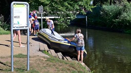 Menschen hieven an einem Bootsanlegesteg an der Niers in der Innenstadt von Weeze am 05.08.2020 ein Schlauchboot aus dem Wasser. 