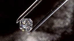Ein Diamant wird von einer Pinzette gehalten, im Hintergrund Nebel, unscharf