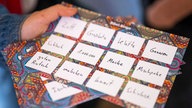 Eine Frau verkauft bei einem Jüdischen Straßenfest Karten mit Ausdrücken auf Jiddisch für ein Bingo-Spiel.