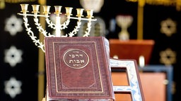 Ein jüdisches Gebetsbuch steht in der neuen Synagoge des Jüdisch-Bucharisch-Sefardischen Zentrums in Hannover vor einer Menora