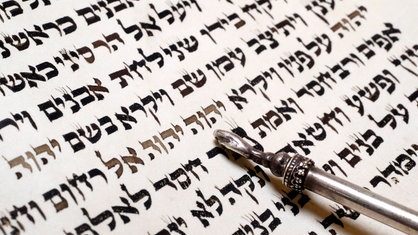 Ein ritueller Zeigestab deutet in einer Tora-Schrift auf hebräische Schriftzeichen