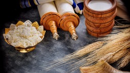 Kornähren, Frischkäse und Milch liegen mit einer Tora und einem Schofar-Horn auf einem Tisch