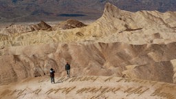 Wüstenlandschaft mit zwei Personen und unleserlicher Schrift auf dem Boden.