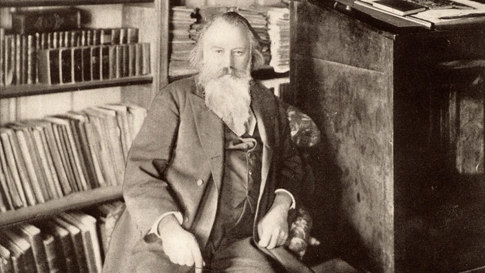 Der Komponist Johannes Brahms sitzt in seiner Bibliothek