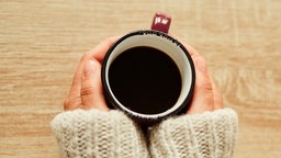 Eine Frau hält eine auf dem Tisch stehende Kaffeetasse in ihren Händen