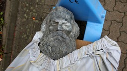 Wie mit einer Decke zugedeckt: Eine liegende Karl Marx-Statue mit einer bis zu den Schulter hochgezogenen Abdeckung.