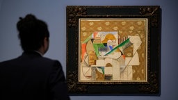 Gitarre und Notenblatt von Pablo Picasso hängt in der Ausstellung, ein Besucher schaut sich das Kunstwerk an. 