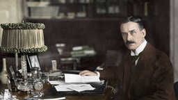 Kolorierte Aufnahme von Thomas Mann am Schreibtisch.