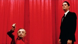 Filmstill aus Twin Peaks: Agent "Dale Cooper" (Kyle MacLachlan) mit "dem Mann von einem anderen Ort" (Michael J. Anderson) in ein roten Zimmer.