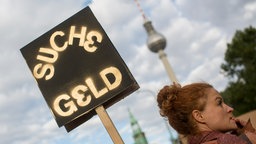 Symbolbild: "Suche Geld" steht am 28.09.2013 auf dem Schild einer Demonstrantin in Berlin, während im Hintergrund der Fernsehturm zu sehen ist.