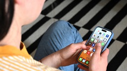 Eine Jugendliche sitzt auf dem Boden und nutzt ein Smartphone - auf dem Display sind verschiedene Apps zu sehen.