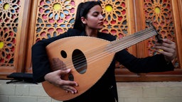 Eine junge iranische Musikerin mit dunklen Haaren, hält eine Oud in der Hand und stimmt sie.