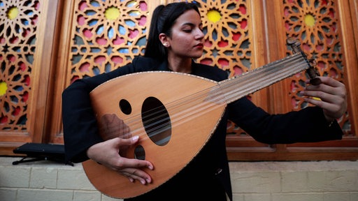 Eine junge iranische Musikerin mit dunklen Haaren, hält eine Oud in der Hand und stimmt sie.