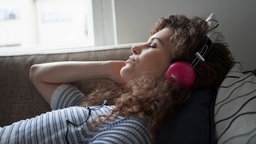 Eine junge Frau liegt auf dem Sofa und hört über Kopfhörer Musik.