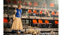 Szenenfoto von Giuseppe Verdis Oper "Der Troubadour" in Bielefeld: Eine Person mit Rüstung steht inmitten von menschlichen Knochen und Schädeln vor fast leeren Stuhlrängen.