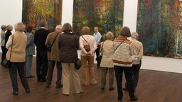 Seniorinnen und Senioren stehen vor drei Gemälden in einem Museum 