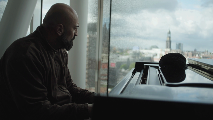 Cover zur Doku-Serie „XATAR – Ein Leben ist nicht genug“: Xatar sitzt an einem Klavier.