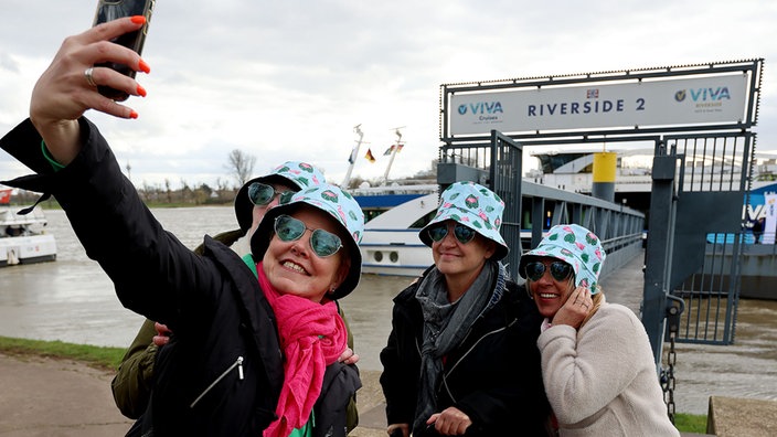 Vier Mitreisende mit Herzchen-Sonnenbrillen machen vor Abreise ein Selfie vor dem Schiff