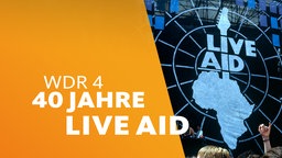  Live-Aid-Festival 1985 Wembley: Blick auf die Bühne, Menschenmenge im Vordergrund, rechts groß das Logo der Aktion