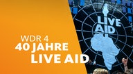  Live-Aid-Festival 1985 Wembley: Blick auf die Bühne, Menschenmenge im Vordergrund, rechts groß das Logo der Aktion