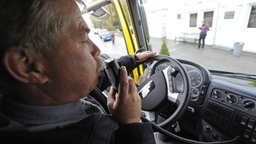Ein Mann pustet in einen Alkolok, das die Zündung außer Kraft setzt, sobald der Fahrer unter Alkoholeinfluss steht