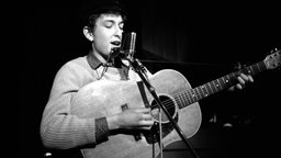 Bob Dylan steht bei einem Auftritt im Jahr 1962 mit Gitarre und Mundharmonika auf der Bühne