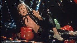 Der belgische Musiker Plastic Bertrand posiert leichtbekleidet auf der Bühne (Aufnahme vermutlich aus den 80er Jahren)