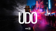 Udo Lindenberg von hinten vor Leuchtreklame und sw-Himmel mit Wolken