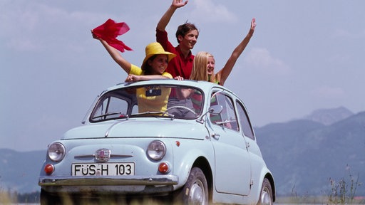 70er Jahre: Drei Menschen winken aus dem Dach eines Autos