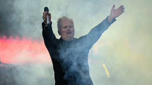 Sänger Herbert Grönemeyer steht beim Auftakt der Tournee 40 Jahre "4630 Bochum" 2024 im Dresdner Rudolf-Harbig-Stadion auf der Bühne und reckt die Arme in die Höhe