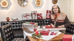 Guildo Horn sitzt an einem Tisch umringt von Geschenken und Geschenkpapier
