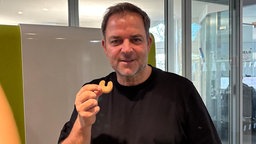 Martin Rütter in einem schwarzem T-Shirt hält ein Vanillekipferl hoch. 
