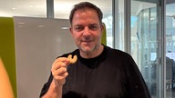 Martin Rütter in einem schwarzem T-Shirt hält ein Vanillekipferl hoch. 