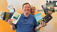 Mike Altwicker und Heike Knispel stehen im WDR 4-Studio und halten acht Bücher in den Händen