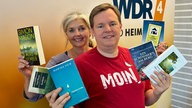 Mike Altwicker und Heike Knispel mit den sechs Krimitipps in den Händen vor einer orangenen WDR 4-Wand