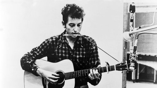 Bob Dylan mit einer Mundharmonika um den Hals und einer Gitarre in den Armen (1941).