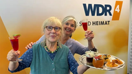Ulla Scholz mit Heike Knispel stehen mit einem Tablett voller Essen im WDR 4 Studio.