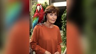 Auf der Schluter von Thekla Carola Wied sitzt ein großer Ara-Papagei, sie schaut leicht verängstigt