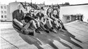 Schwarz-weiß Foto der Band Brings. Sie sitzen auf einem Hausdach, im Hintergrund sind weitere Häuser zu sehen. 
