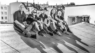 Schwarz-weiß Foto der Band Brings. Sie sitzen auf einem Hausdach, im Hintergrund sind weitere Häuser zu sehen. 