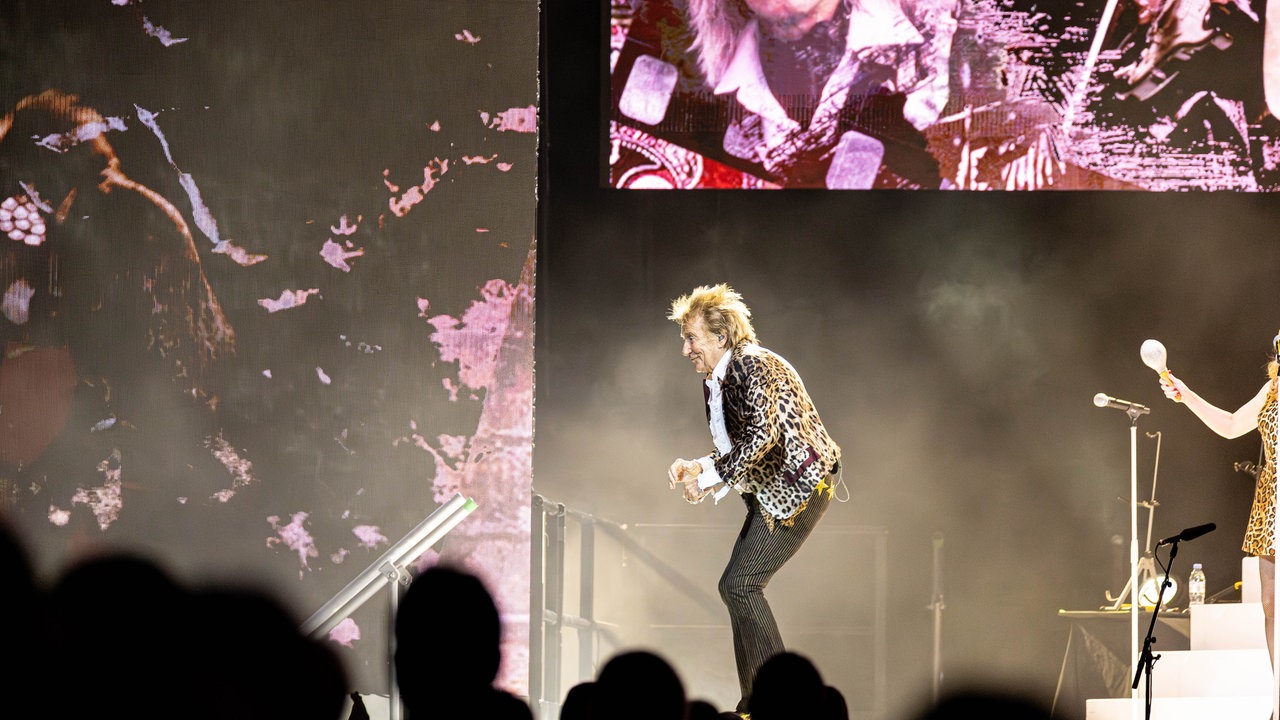 Rod Stewart tanzt auf einer Bühne in Köln und guckt das Publikum auf der linken Seite an 
