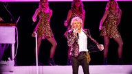 Rod Stewart hat ein Mikrofon in der Hand und singt auf einer Bühne in Köln