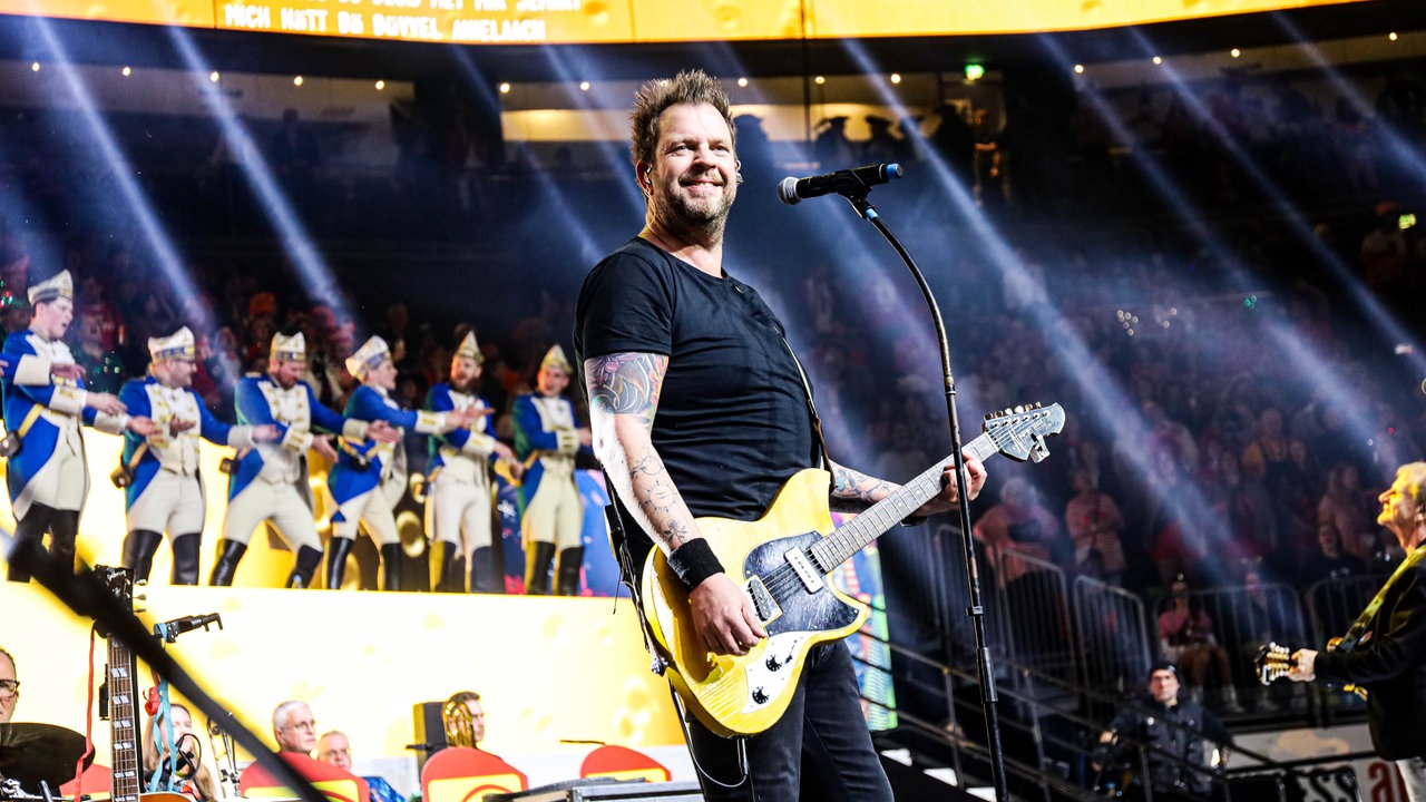 Lachende Köln Arena 2026: Der Sänger der Band Paveier steht lächelnd auf der Bühne