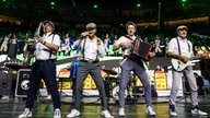 Lachende Köln Arena 2026: Vier Musiker der Band Klingelköpp stehen mit ihren Instrumenten in einem weißen Hemd und Schiebermütze auf der Bühne